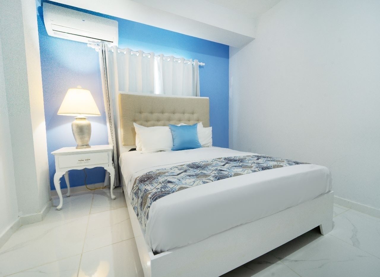 A bedroom with a bed, a nightstand, a lamp, and a window with curtains.