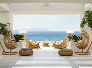 Un salon moderne avec des meubles en osier, une table basse centrale et une vue sur la mer et les montagnes.