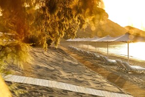 A beach with sun loungers and umbrellas, a wooden boardwalk, and a body of water in the background. - Ikos Aria (Kos)