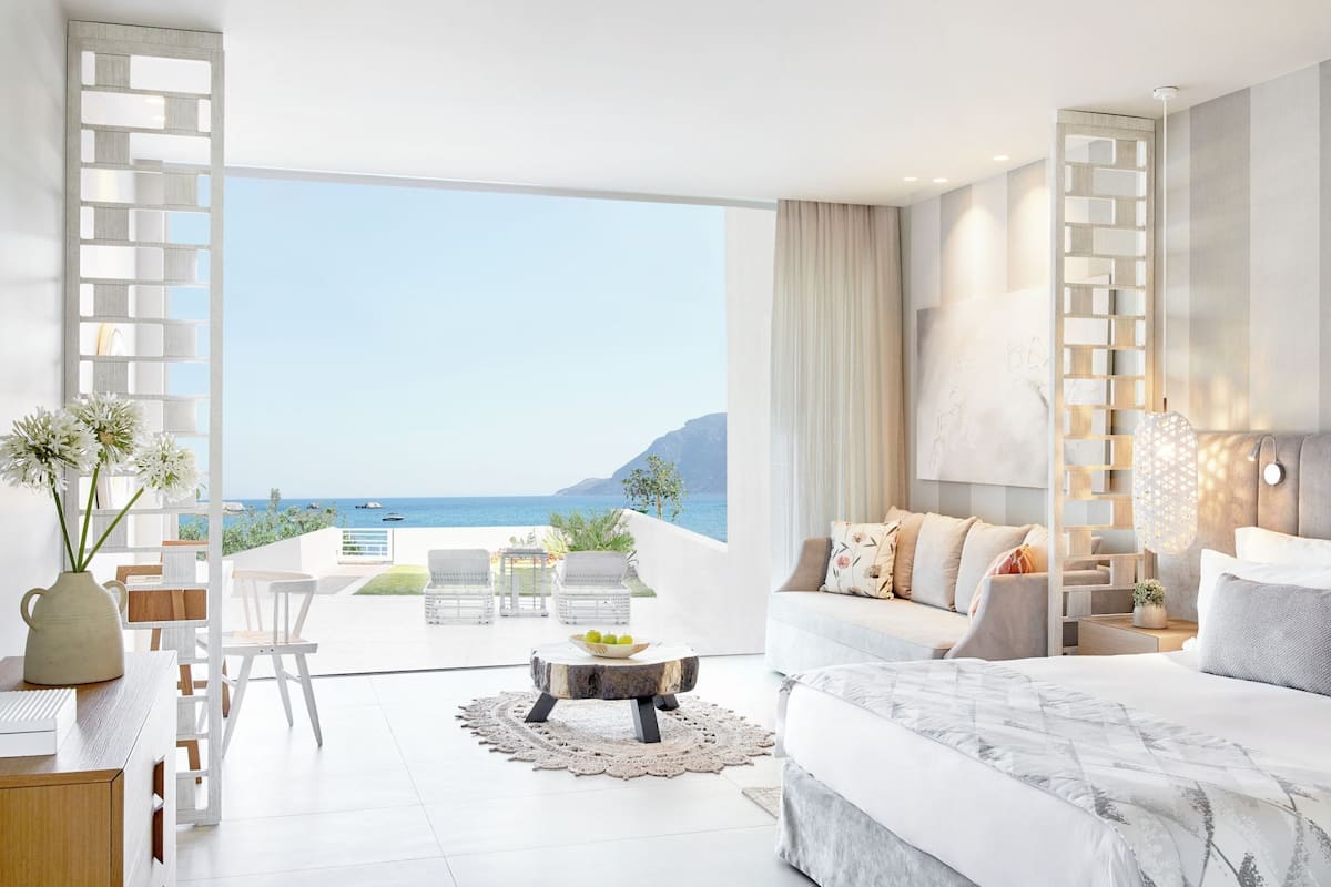Un dormitorio moderno con una cama grande, un balcón con vistas al mar y una zona de comedor con mesa y sillas.