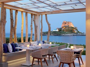 Un área de comedor al aire libre con vistas al mar y una isla rocosa.
