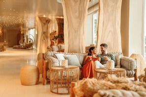 A modern living room with a sofa, wicker ottomans, and a large window. - Ikos Aria (Kos)