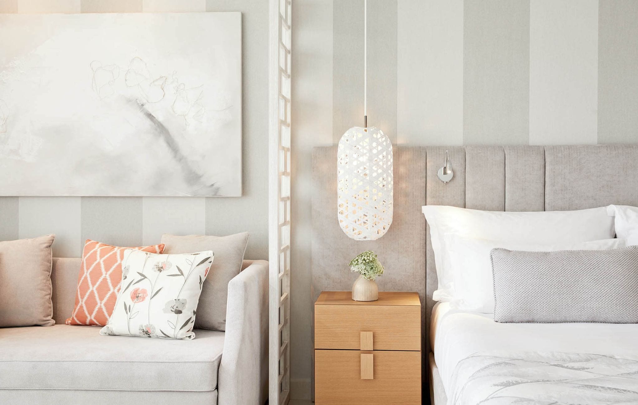 A modern bedroom with a grey sofa, a wooden nightstand, a bed with white bedding, and a hanging light fixture.