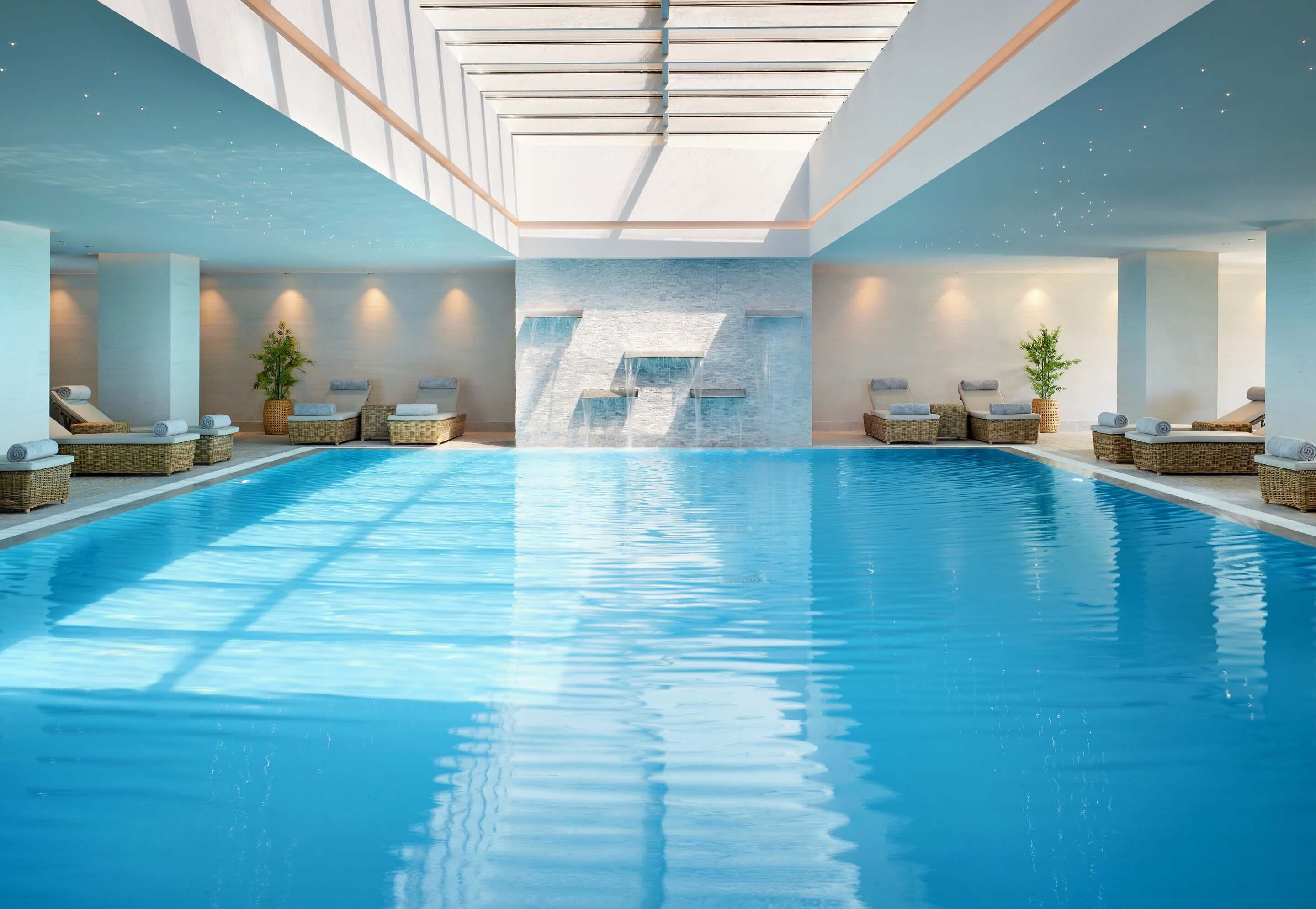 A large indoor swimming pool with multiple lounge areas and a waterfall feature.