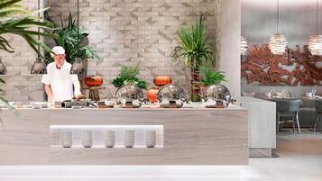 Een moderne keuken met een kok die eten bereidt, een houten aanrecht met keukengerei en een eethoek met stoelen en een tafel.
