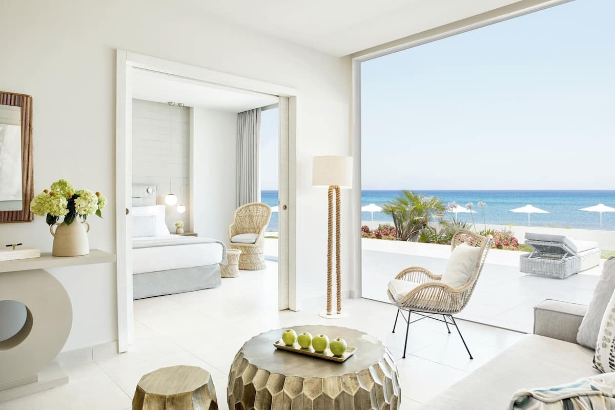 Una habitación de hotel moderna con balcón, cama, zona de estar y vista al océano.