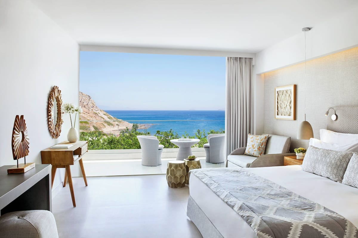 Un dormitorio moderno con una ventana grande, una cama, un escritorio y una zona de estar con vista al océano.