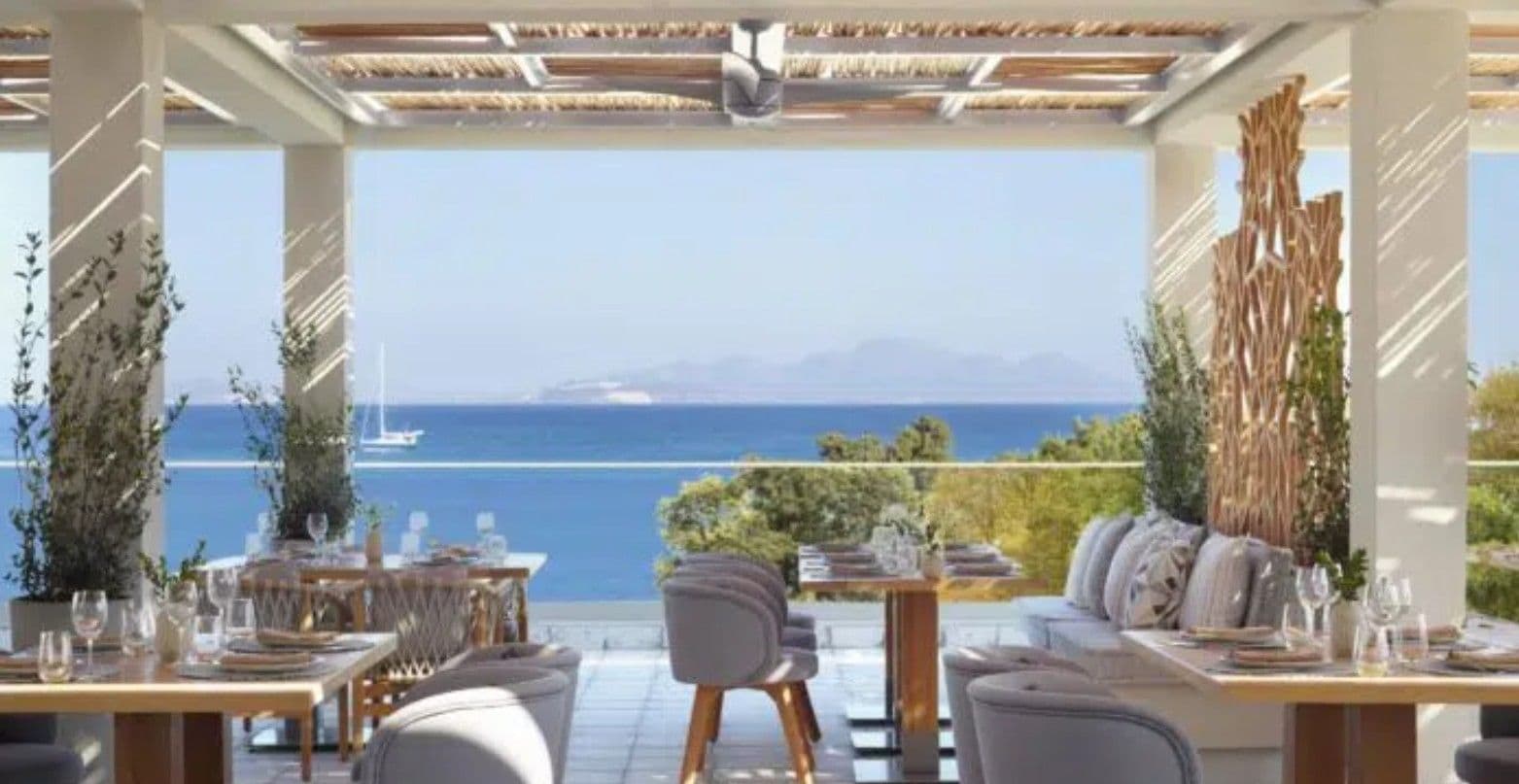 An outdoor dining area with tables set for two, overlooking a body of water and distant land.