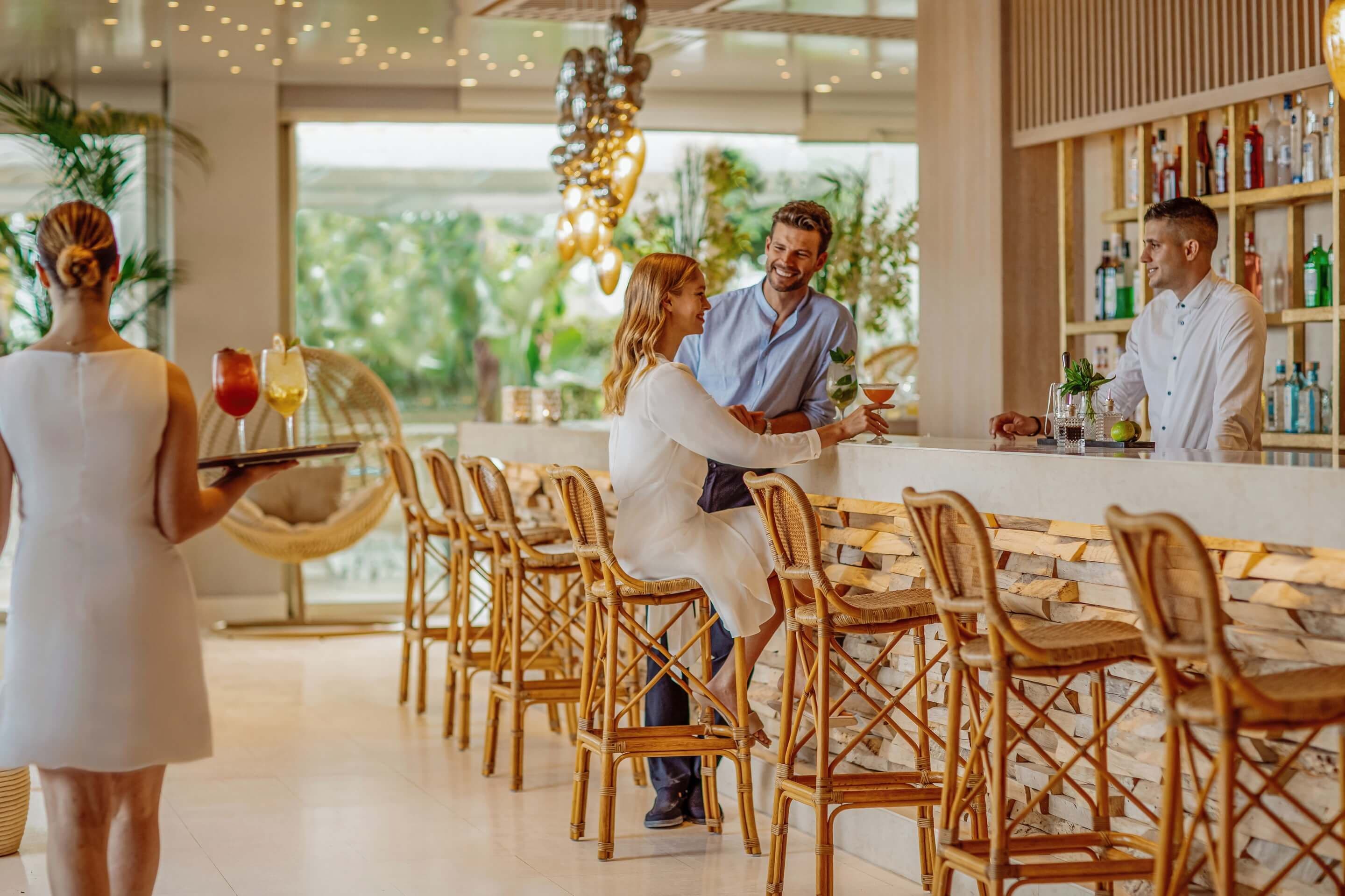 A bar area with wicker chairs, a bar counter, and a bartender.