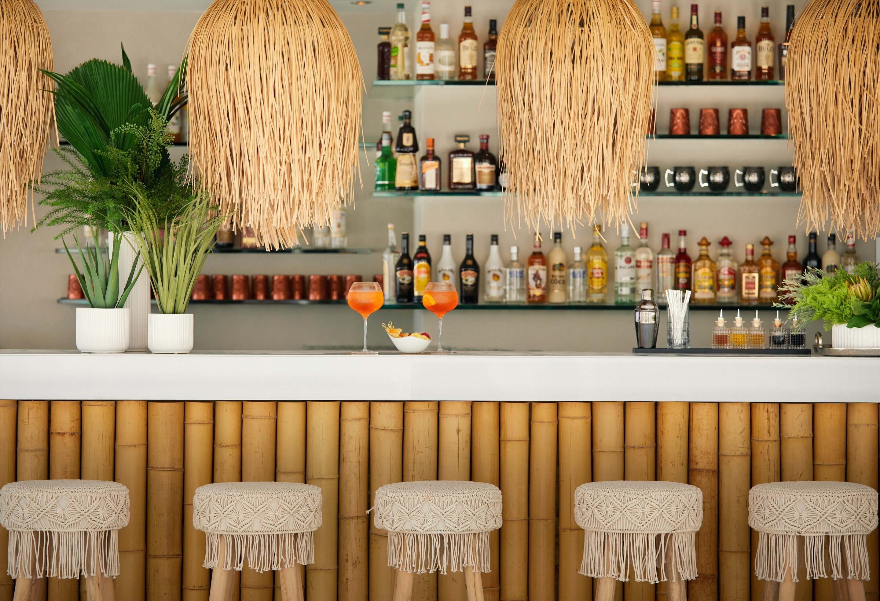 Een barruimte met geweven verlichtingsarmaturen, flessen aan de bar en krukken van macramé.