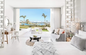 Una habitación de hotel moderna con balcón, una cama, un sofá, un escritorio y vistas a una piscina y palmeras.
