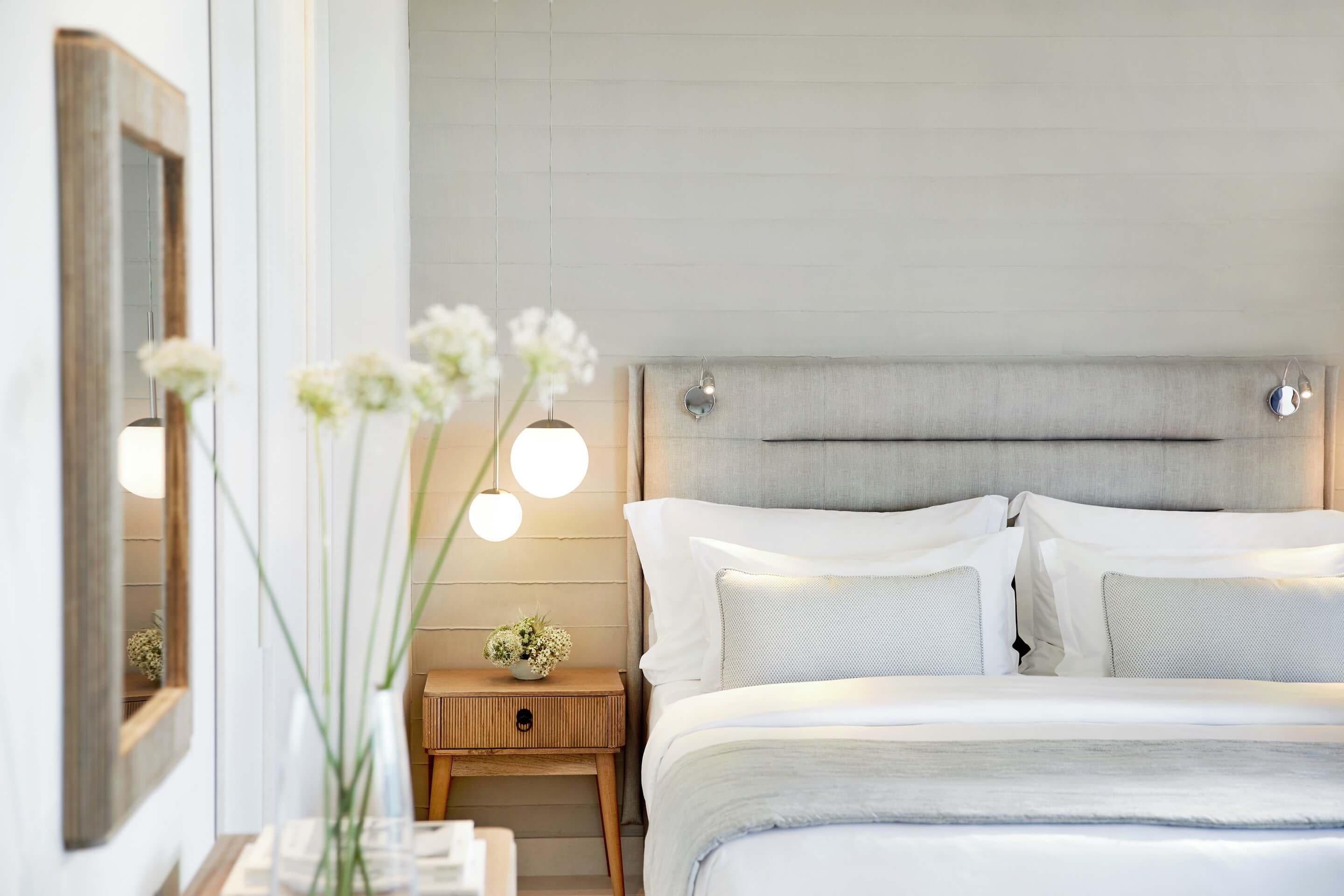 Een slaapkamer met een bed, nachtkastje, lamp en spiegel.