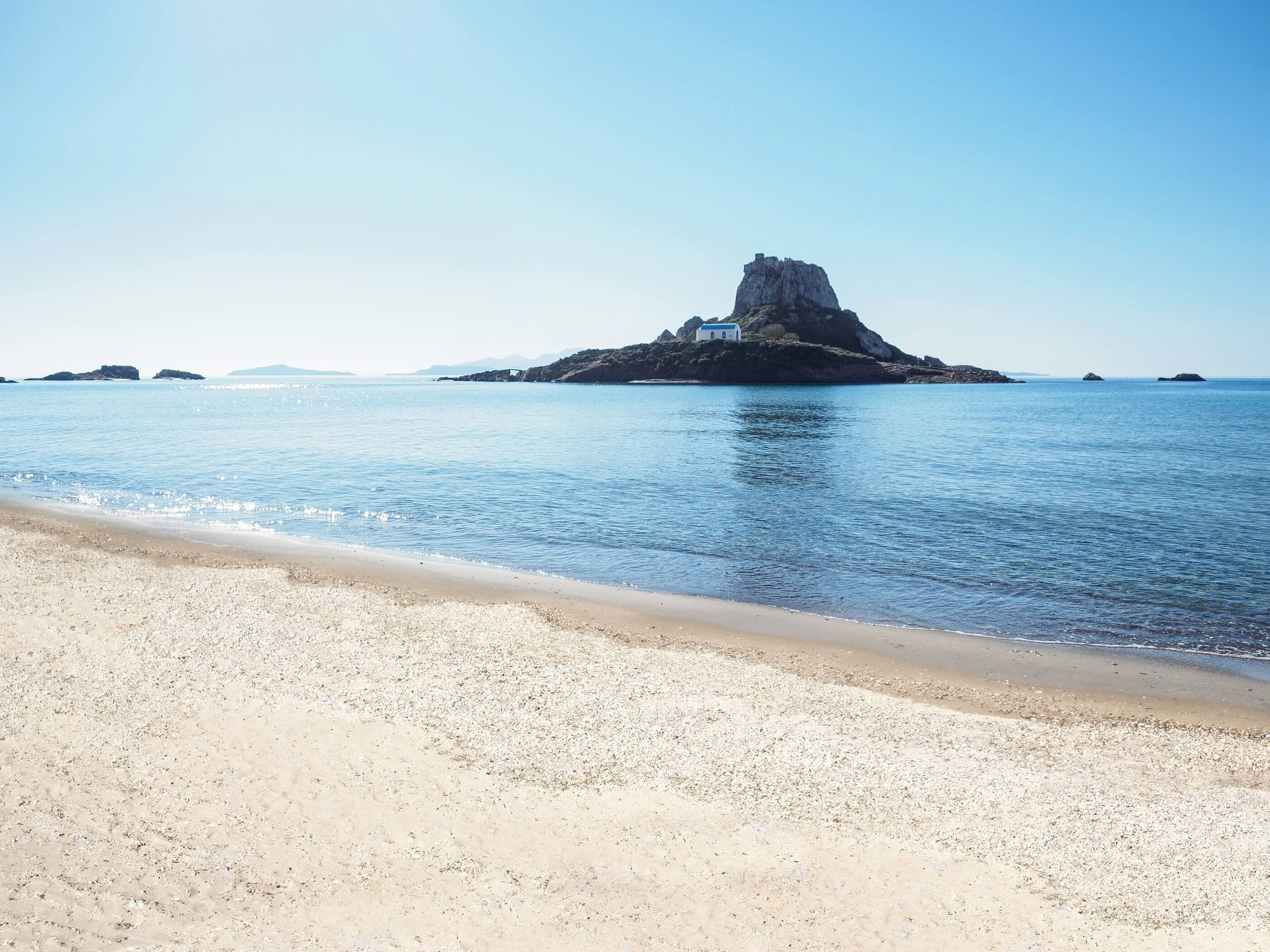 Una spiaggia con un'isola rocciosa e un piccolo edificio.