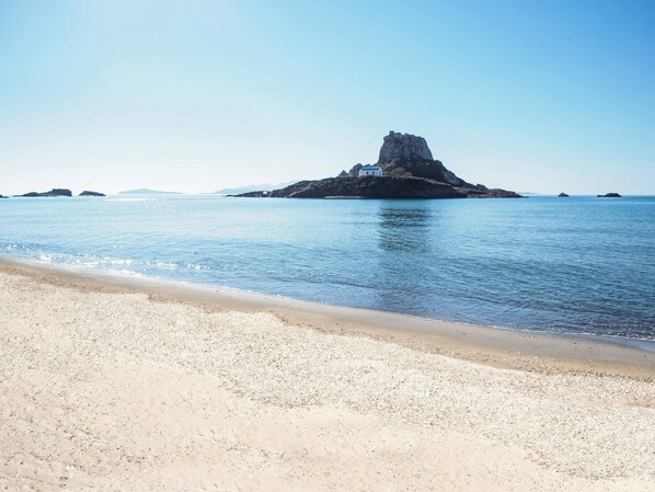 Une plage avec une île rocheuse et un petit bâtiment.