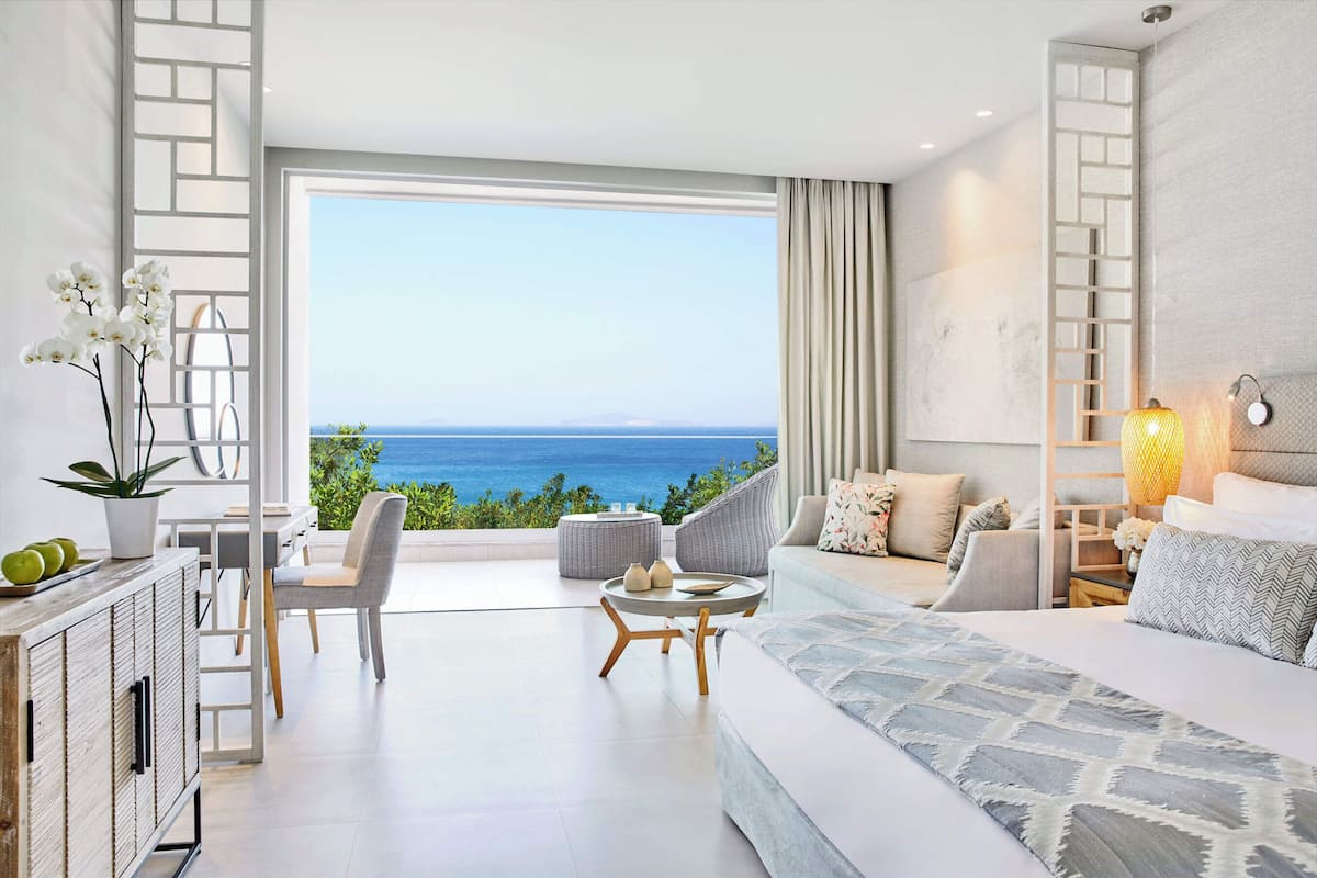 Una habitación de hotel moderna con balcón, cama, zona de estar y vista al océano.