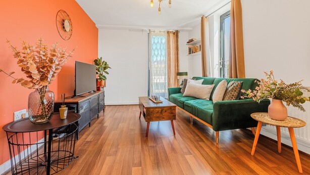 Ett vardagsrum med en grön soffa, ett soffbord i trä, en tv och en vas med blommor.
