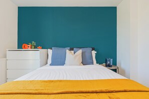 Ein Bett mit weißer Bettwäsche, eine türkisblaue Wand und ein kleiner Tisch mit einer blauen Kerze.