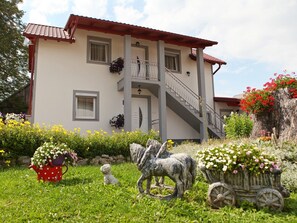 Ein zweistöckiges Gebäude mit einem Balkon, einer Treppe und einem Garten mit Blumen und einer Statue.