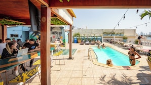 Un área de piscina en la azotea con sillones de descanso, una piscina y un comedor con mesas y sillas.