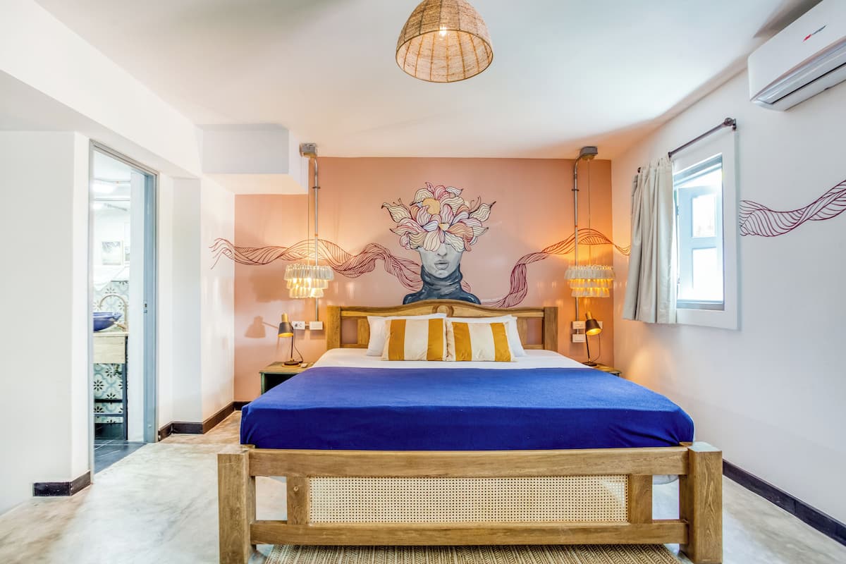 A bedroom with a bed, a wall mural, bedside lamps, and an air conditioning unit.
