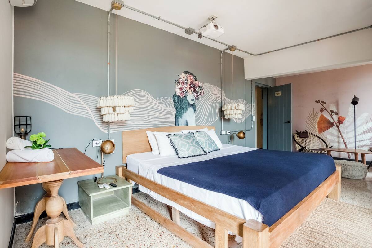 A hotel room with a bed, bedside table, lamp, and a wall mural.