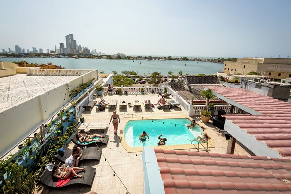 Una piscina en la azotea con vistas al horizonte urbano, sillas de descanso y plantas en macetas.