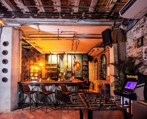 Eine Bar mit einer Tischfußballmaschine, Barhocker und Flaschenregalen.