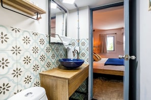 Un baño con un lavabo azul, un tocador de madera, un inodoro y un espejo.