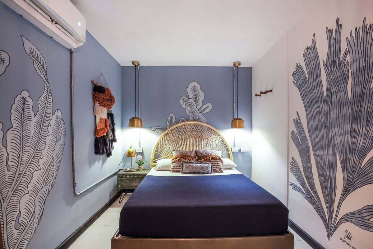 A bedroom with a bed, wall art, and a hanging plant.