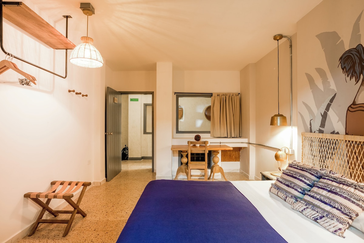 A hotel room with a bed, desk, chair, and a large mirror.