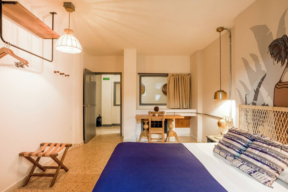 A hotel room with a bed, desk, chair, and a large mirror.