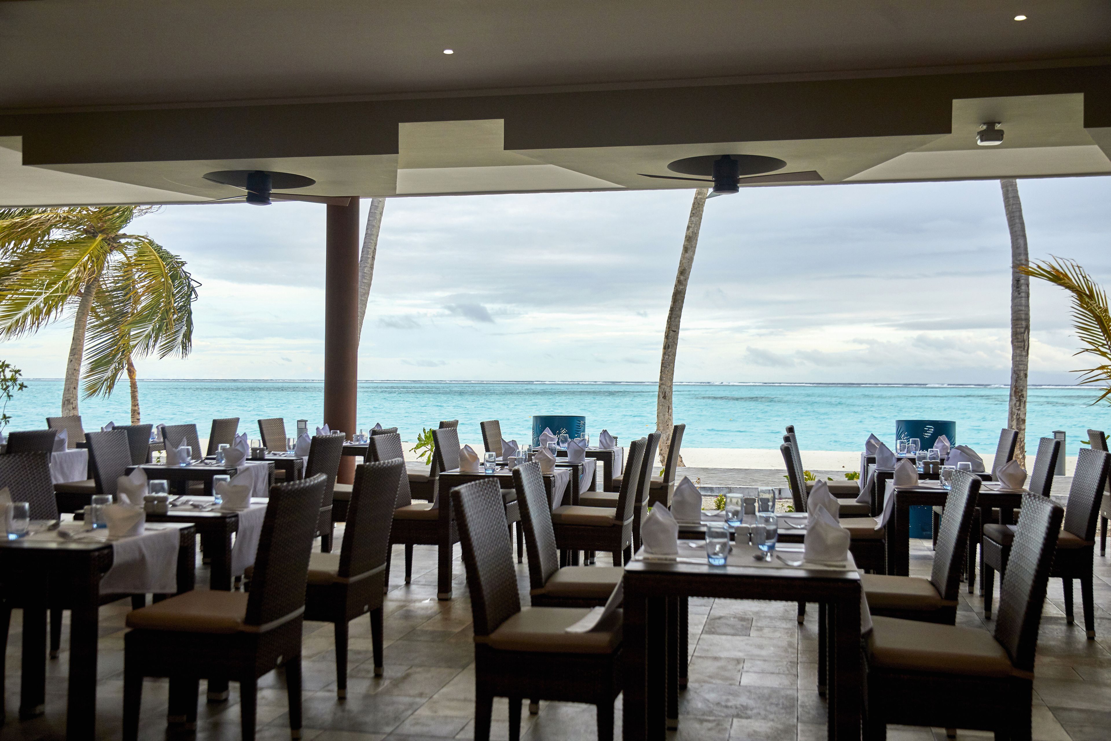 An outdoor dining area with tables and chairs, overlooking a beach and ocean.