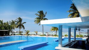 A pool area with clear blue water, palm trees, and a view of the beach.