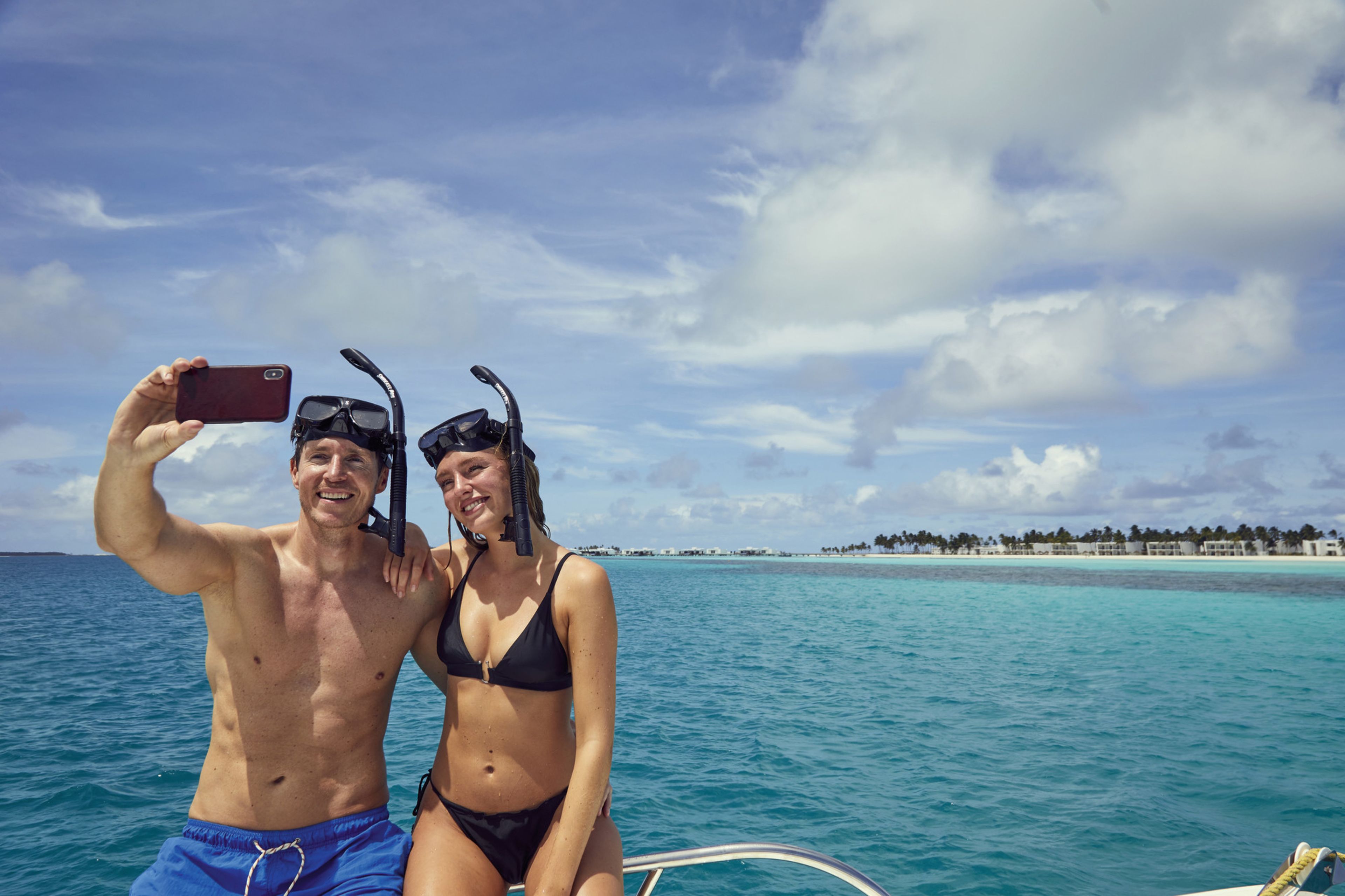 Two people on a boat in a clear blue sea with a distant shoreline.