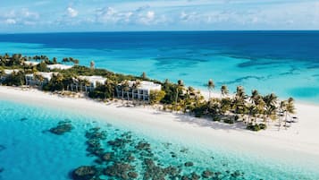 Vista aérea de um resort na praia com águas azul-turquesa cristalinas, areia branca e palmeiras.
