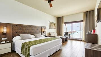 Habitación de hotel con una cama grande, un escritorio, una silla, un ventilador de techo y vistas al mar a través de las ventanas.
