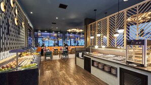 A buffet area with a variety of food items, a seating area with tables and chairs, and a view through large windows.