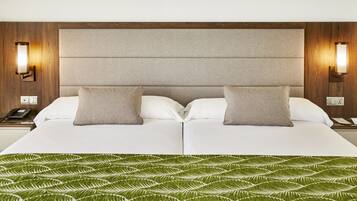 Cama de casal com manta estampada em folhas verdes, duas almofadas e cabeceira de madeira com arandelas.