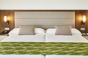 A double bed with a green leaf-patterned throw, two pillows, and a wooden headboard with wall sconces. - Hotel Riu Atoll (Kedhigandu)