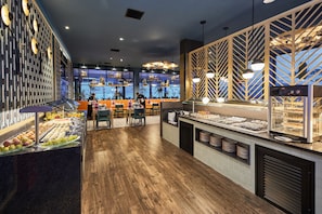 A buffet area with a variety of food items, a seating area with tables and chairs, and a view through large windows. - Hotel Riu Atoll (Kedhigandu)