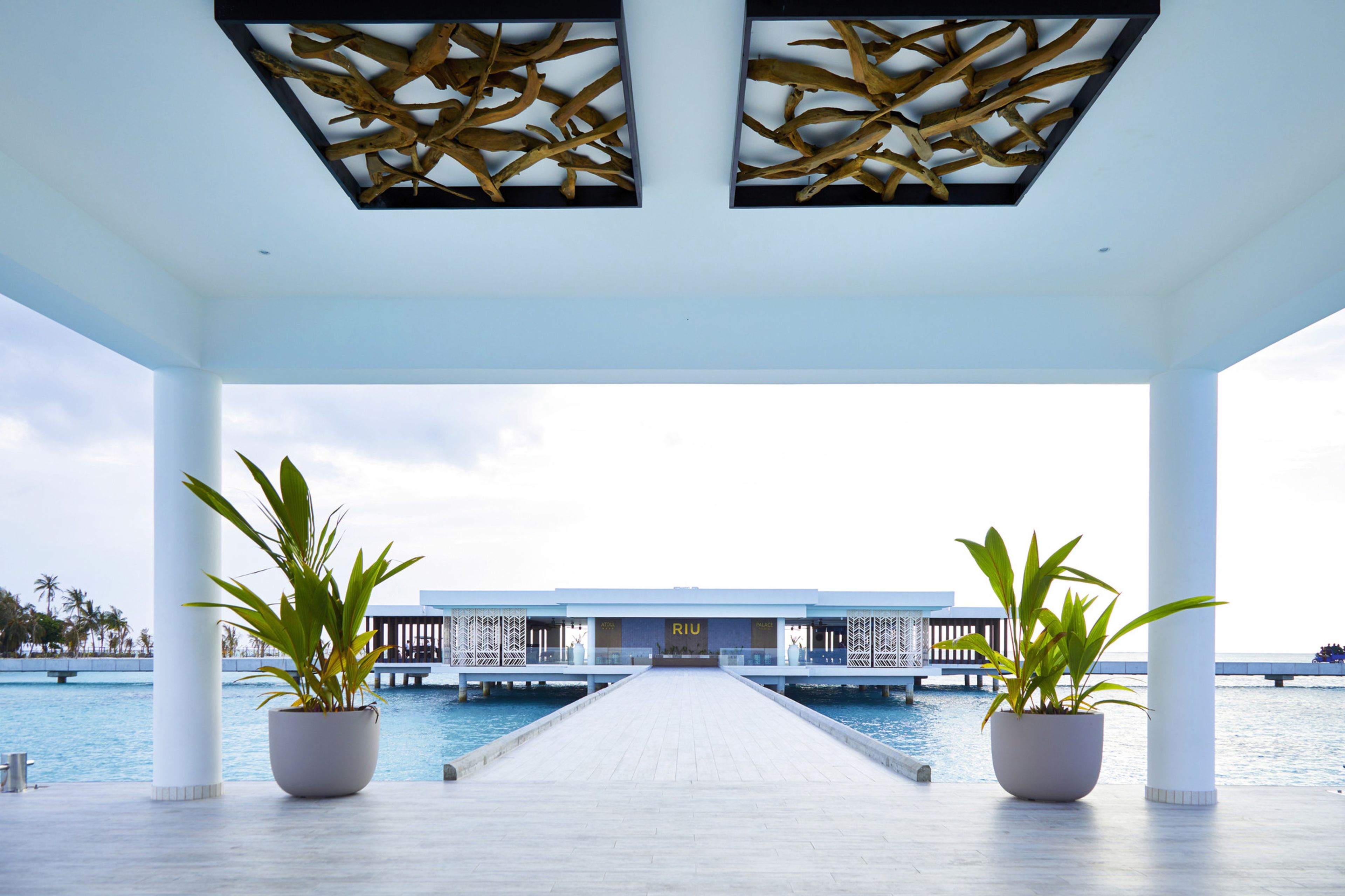 Uma galeria coberta que leva a um edifício com a placa "RIU", em frente a uma piscina.