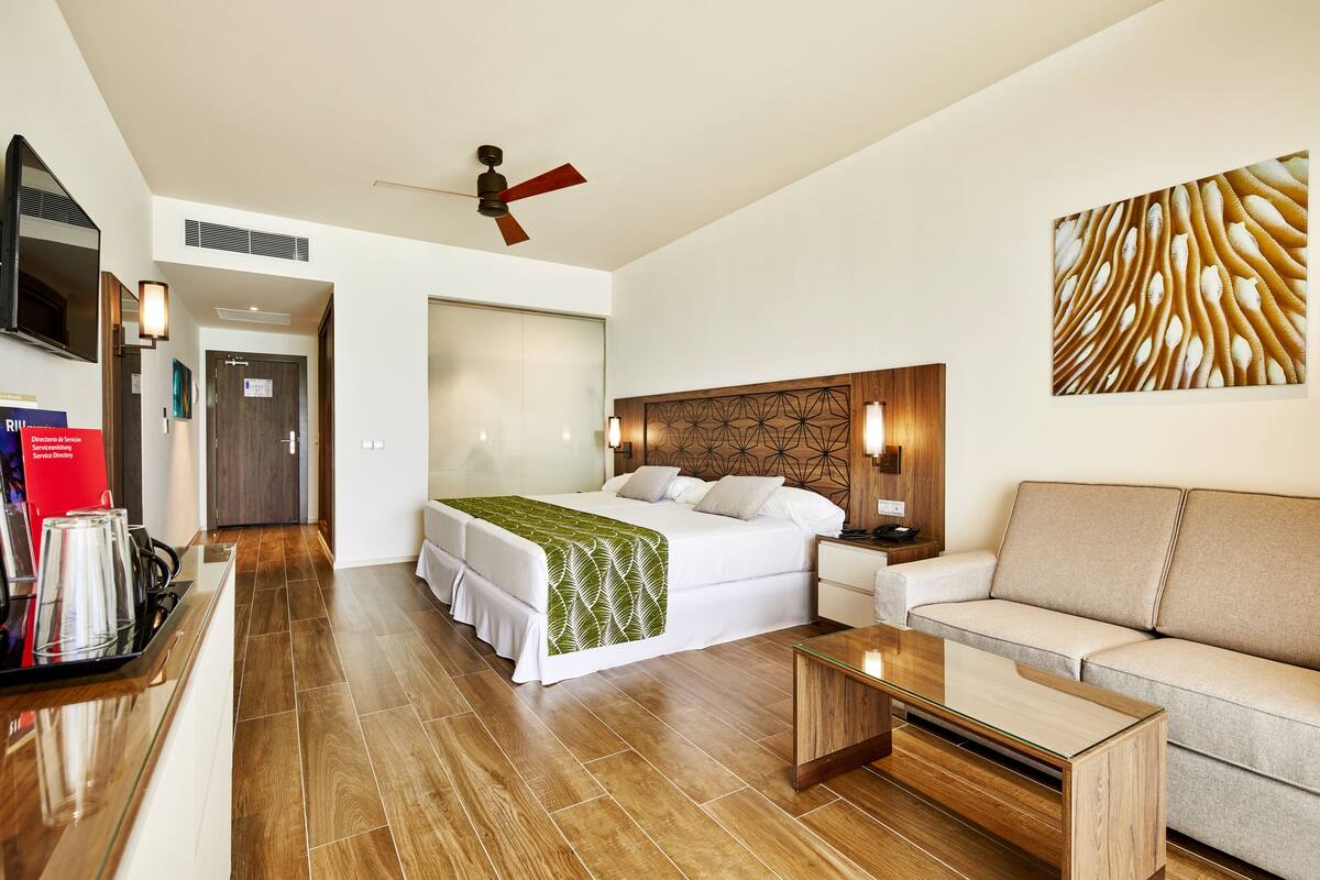 A hotel room with a bed, a sofa, a coffee table, a TV, and a ceiling fan.