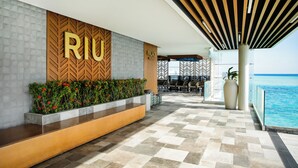 A modern hotel lobby with a 'RIJU' sign, a pool area, and outdoor seating.