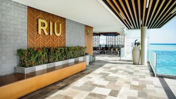 A modern hotel lobby with a 'RIJU' sign, a pool area, and outdoor seating.
