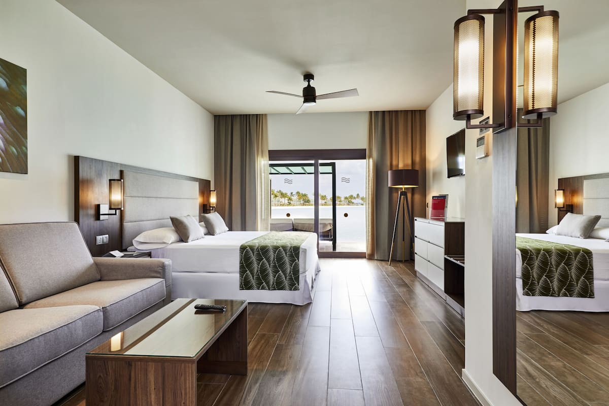 A hotel room with two beds, a sofa, a coffee table, and a ceiling fan.
