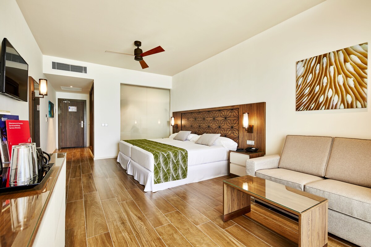 Una habitación de hotel con cama, sofá, mesa de centro, televisor y ventilador de techo.