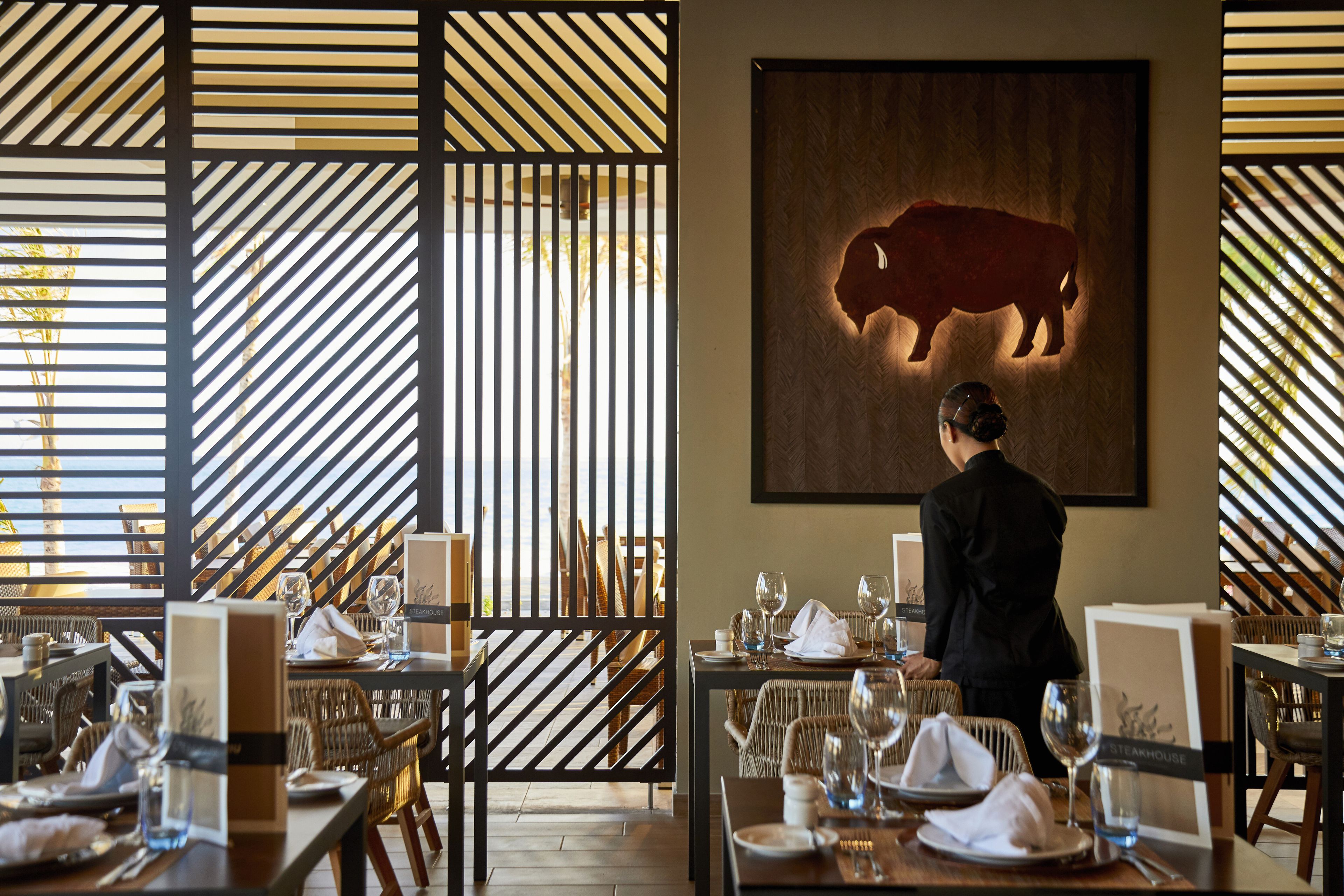 Un ristorante con una sala da pranzo con tavoli apparecchiati, piatti, bicchieri e posate. Si vede una persona sullo sfondo.