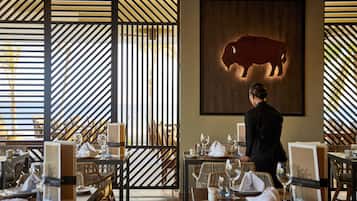 A restaurant with a dining area featuring tables set with plates, glasses, and cutlery. A person is visible in the background.