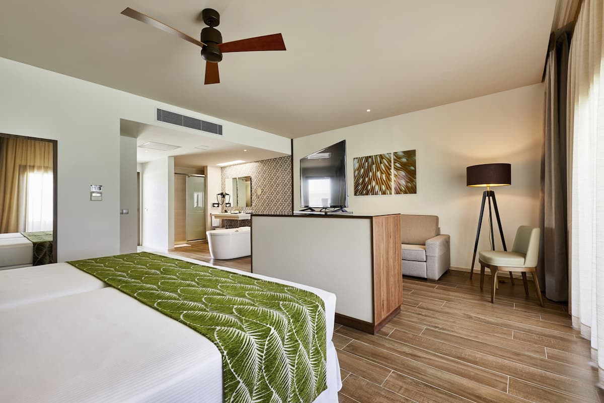 A hotel room with a bed, a desk, a chair, a ceiling fan, and a mirror.
