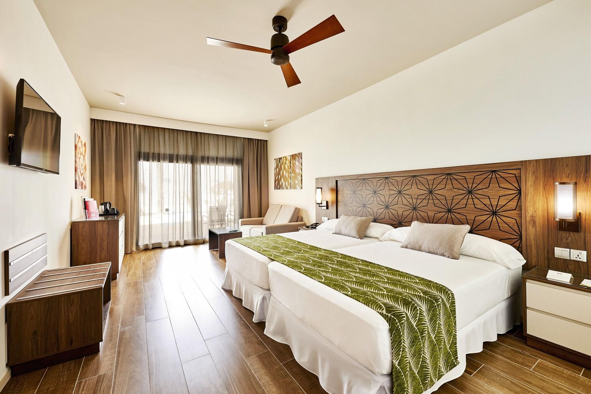 Habitación de hotel con una cama grande, un escritorio, una silla, un televisor y un ventilador de techo.